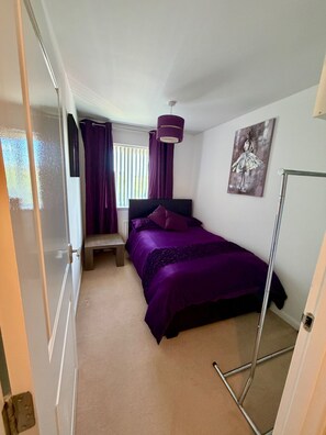A bedroom with a bed, a bench, a painting, a floor lamp, and a window with curtains.