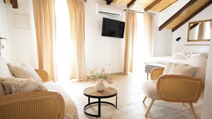 Una stanza con divano, poltrone, un tavolino con fiori, televisione a schermo piatto e ventilatore a soffitto.