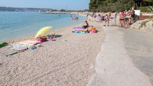 Una spiaggia di ciottoli con persone che prendono il sole e nuotano, un cielo sereno e vista sul mare.