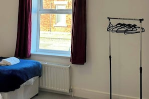 A room with a bed, a window with curtains, a radiator, and a clothes drying rack. - House Sleeps 7 with Parking (Jarrow)