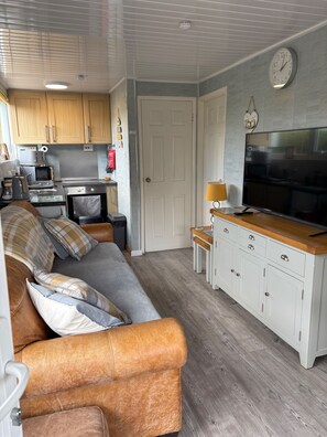 Un espacio habitable compacto con kitchenette, un sofá con cojines, un televisor y un reloj en la pared.