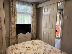 Un dormitorio con cama, televisor en una cómoda, una puerta y vistas al exterior.