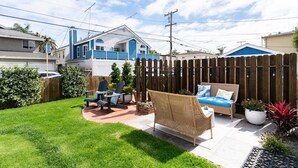 Un jardin avec une clôture en bois, un canapé en osier et deux fauteuils Adirondack.