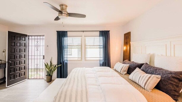 Une chambre à coucher avec un lit, des tables de chevet, un ventilateur de plafond et une fenêtre avec des rideaux.