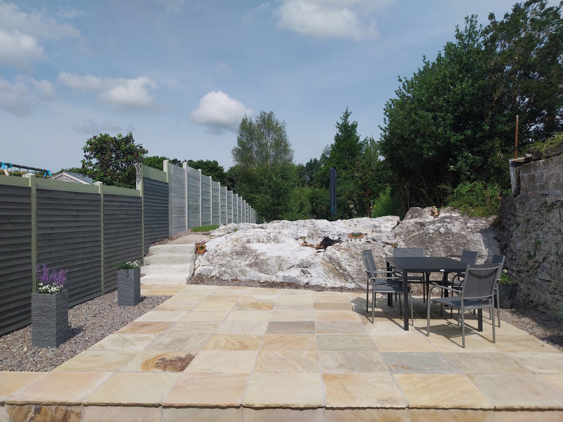 A patio area with stone flooring, a table with chairs, and a stone wall.