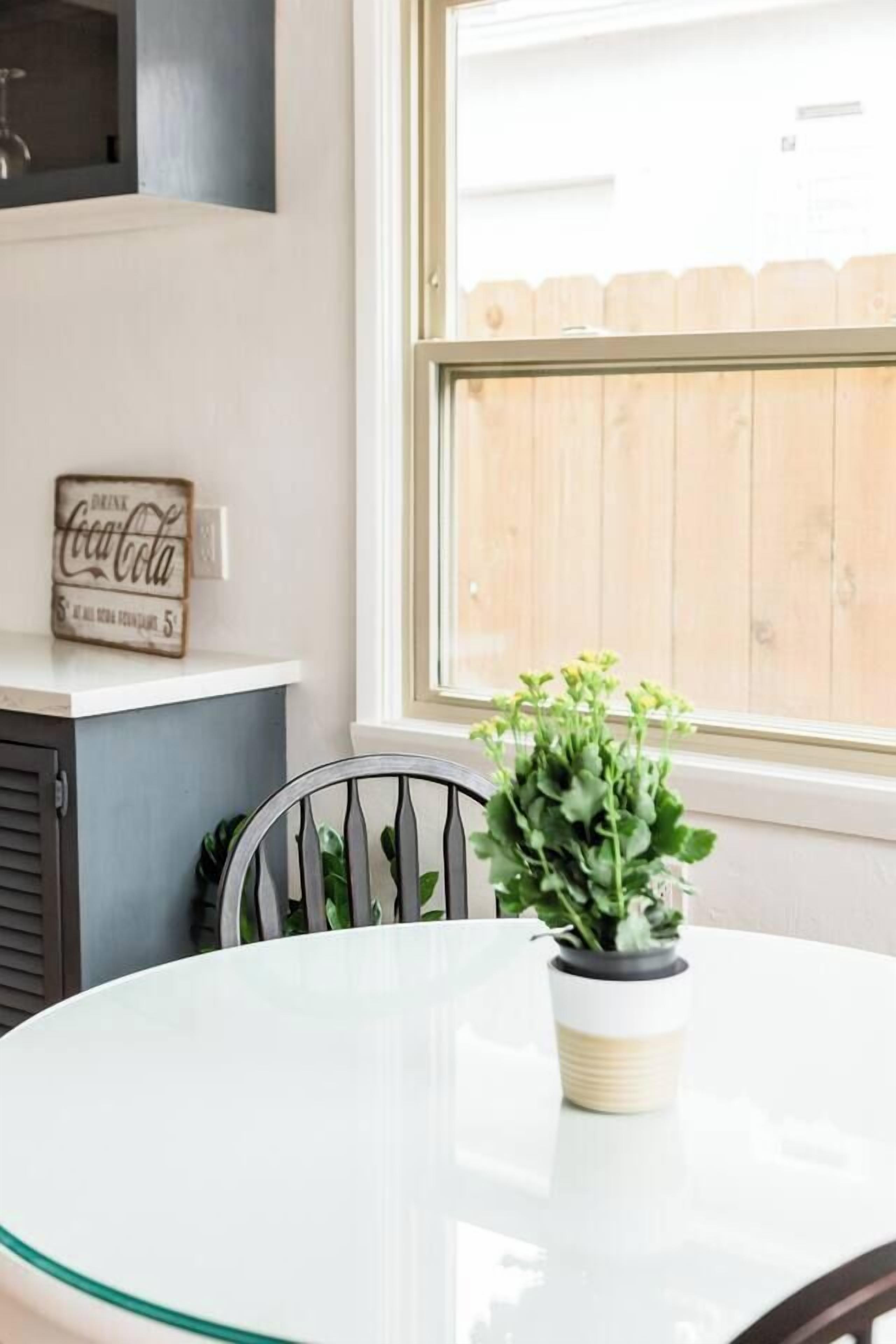 A round glass table with a potted plant, a wall-mounted sign, and a window with a wooden fence outside.