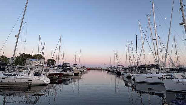 A marina with multiple sailboats docked, calm water, and a clear sky.