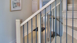 A staircase with a wooden handrail and metal balusters, leading to a landing with a door and a framed abstract painting.