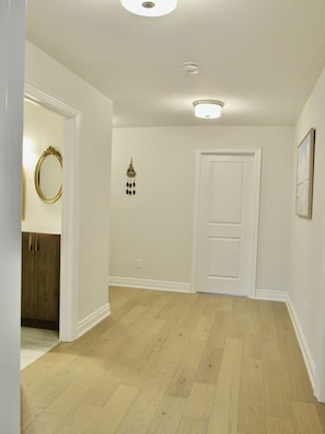 A hallway with wooden flooring, white walls, a door, and a wall-mounted light fixture.