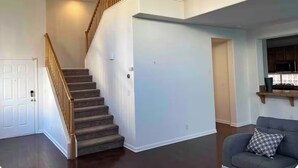 Una escala amb baranes de fusta, una porta blanca i un sofà gris amb un coixí estampat.