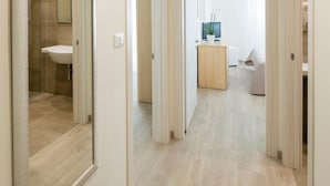 Un couloir avec un miroir, une salle de bain et un espace de vie comprenant un canapé et une petite table.