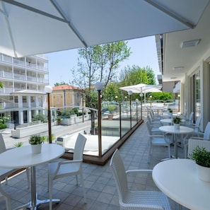 A terrace with outdoor seating, a view of a building with balconies, and a street with parked cars. - Hotel Constellation (Rimini)