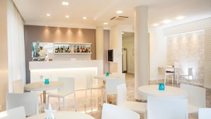 Un hall d’hôtel avec des tables et des chaises rondes, un coin bar avec des étagères remplies de bouteilles et un mur orné de motifs.