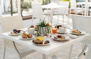 A breakfast table with pastries, fruits, and beverages, surrounded by white chairs and a white table. - Hotel Constellation (Rimini)