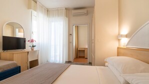 Une chambre d’hôtel comprenant un lit, un bureau avec une télévision, un miroir, une fenêtre avec des rideaux et un appareil de climatisation.