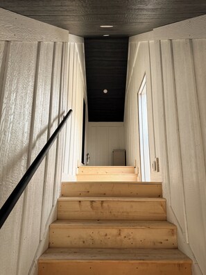 Een houten trap met een zwarte leuning die uitkomt op een plateau.