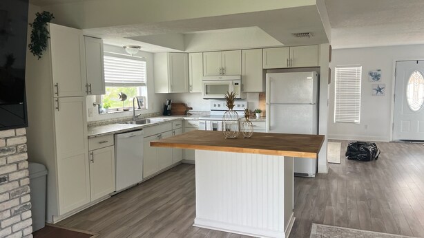 A kitchen with white cabinets, a wooden island, a microwave, and a refrigerator. - The Burnside Bungalow where Vacation Awaits! (Holiday)