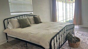 A bed with a metal frame, a patterned rug, and a basket with folded clothes. - The Burnside Bungalow where Vacation Awaits! (Holiday)