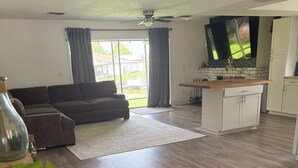 A spacious living area with a sofa, a dining table, and a kitchen area with cabinets and a TV. - The Burnside Bungalow where Vacation Awaits! (Holiday)