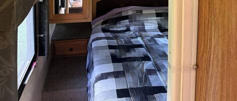 A compact RV bedroom with a bed, wooden cabinets, and a small dresser.