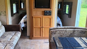 Interior compacto de una caravana con una unidad central de entretenimiento, dos zonas de estar y una pequeña kitchenette.