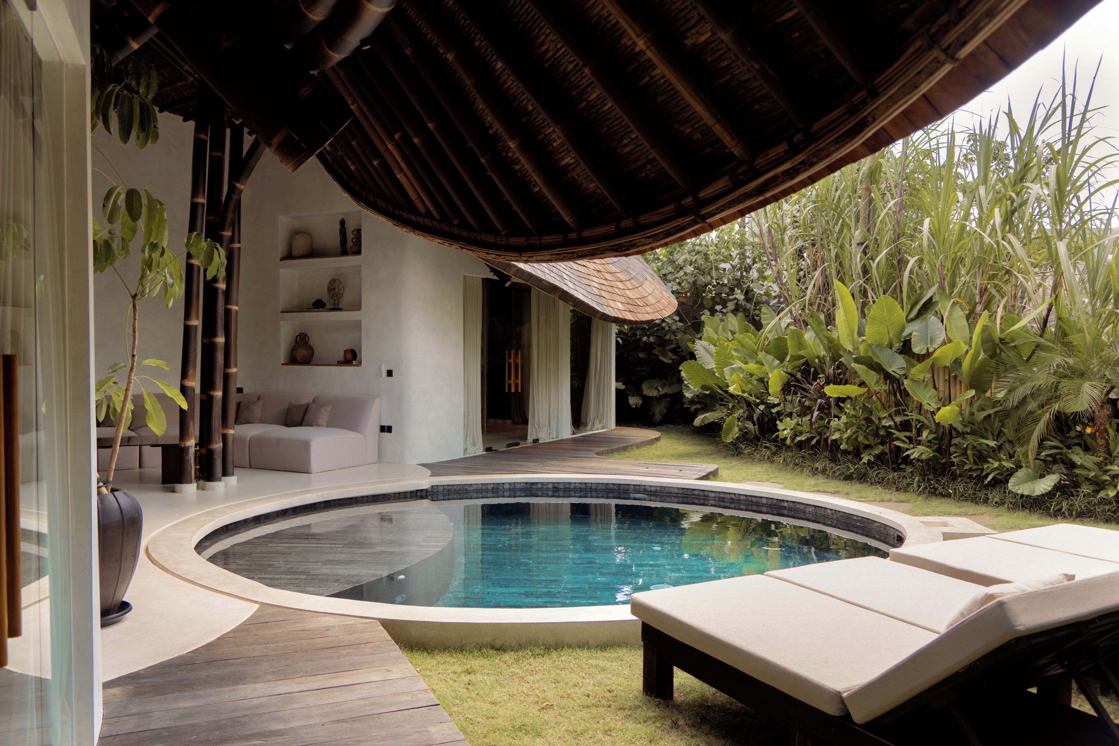 A modern outdoor pool area with a curved design, wooden deck, lounge chairs, and a covered seating area.