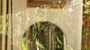 A room with a round mirror, wooden furniture, and a view of greenery outside. - Kaymana (Pecatu)