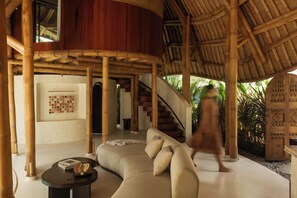 A modern interior with a curved sofa, a round table, and a staircase leading to an upper level. - Kaymana (Pecatu)