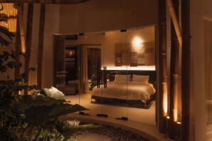 A bedroom with a bed, a glass partition, and a view of a bathroom. - Kaymana (Pecatu)