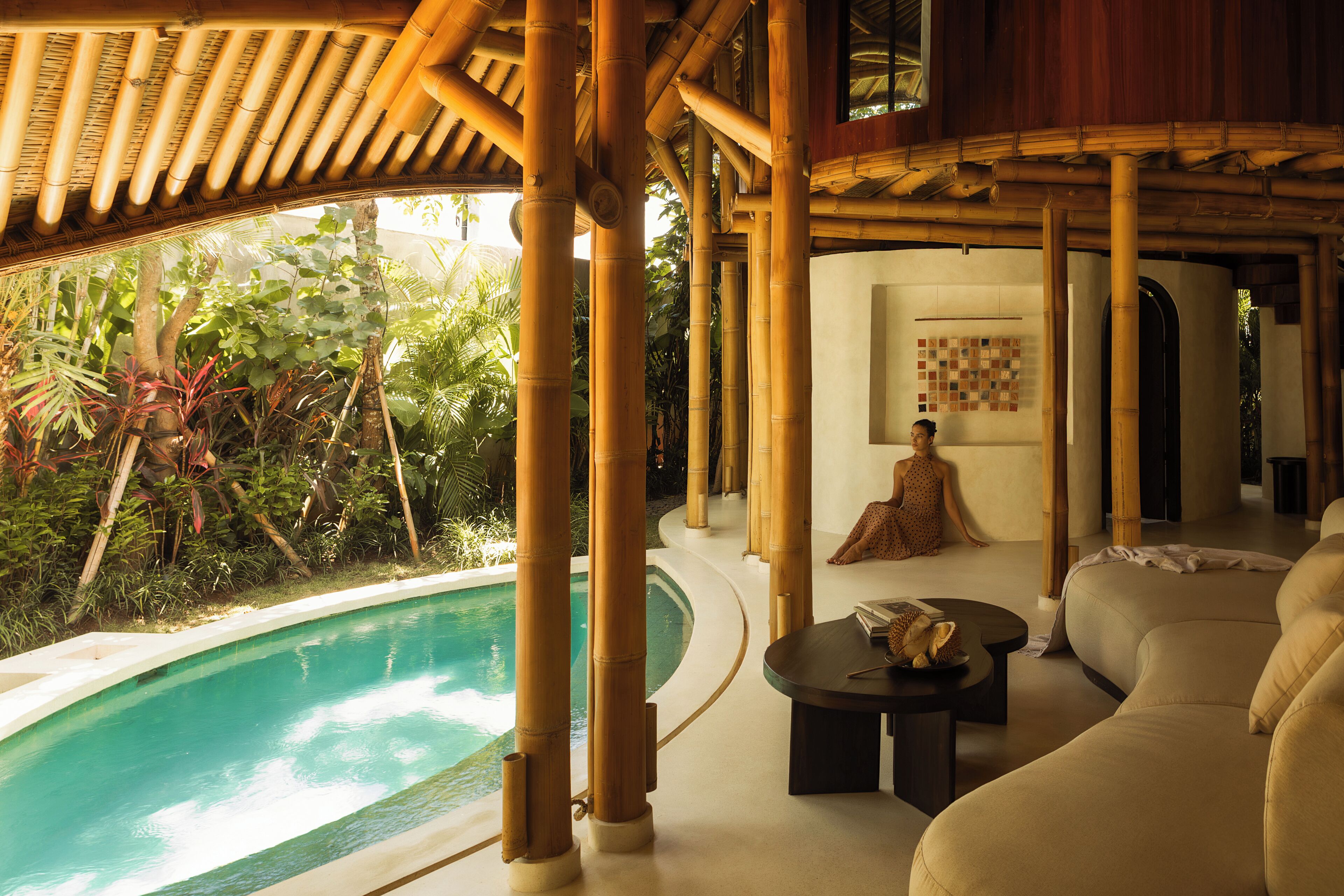 A poolside area with bamboo structures, a sofa, and a person sitting by the pool.