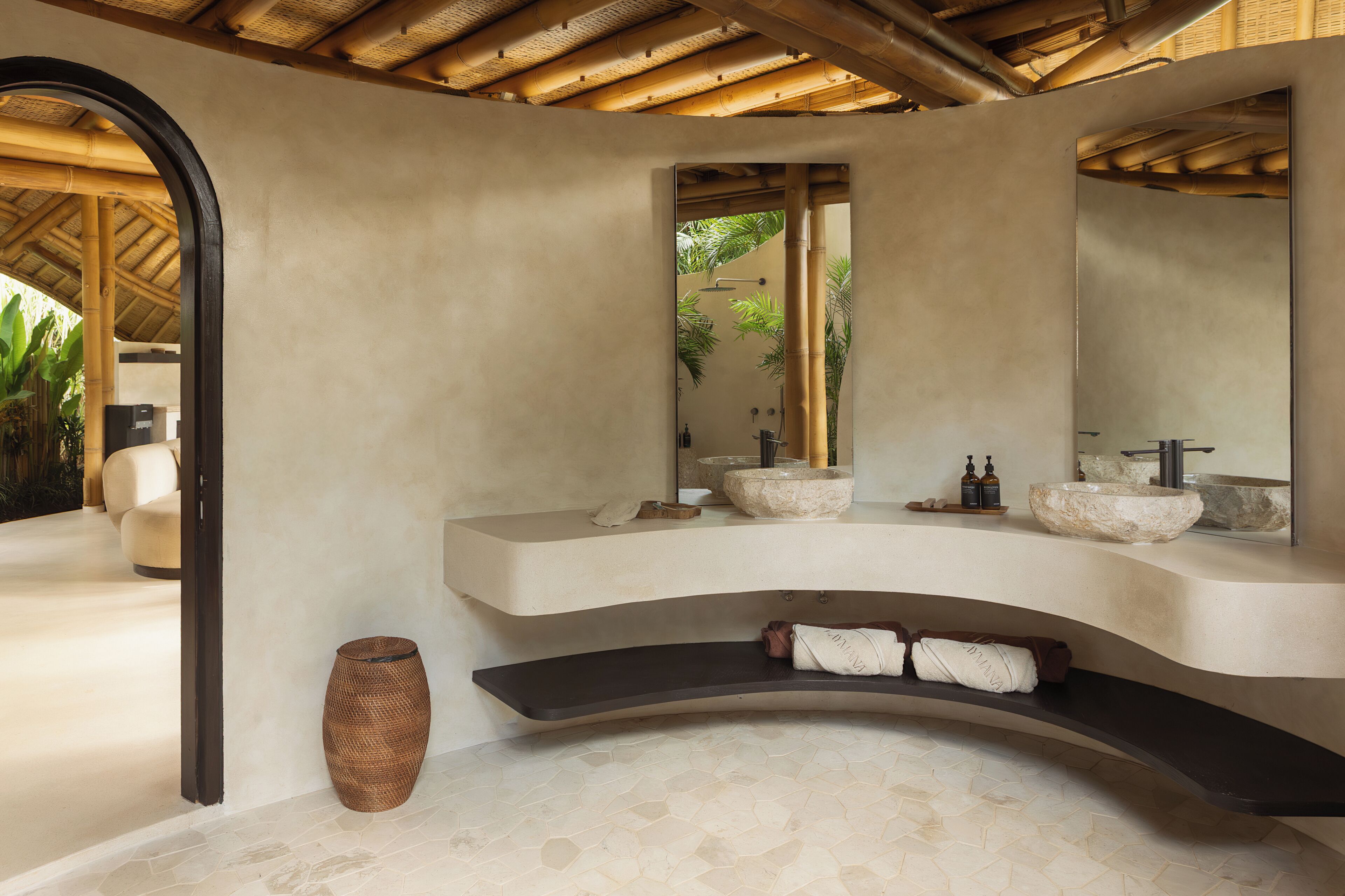 Un baño moderno con un tocador curvo, dos lavamanos, un espejo grande y una cesta tejida.