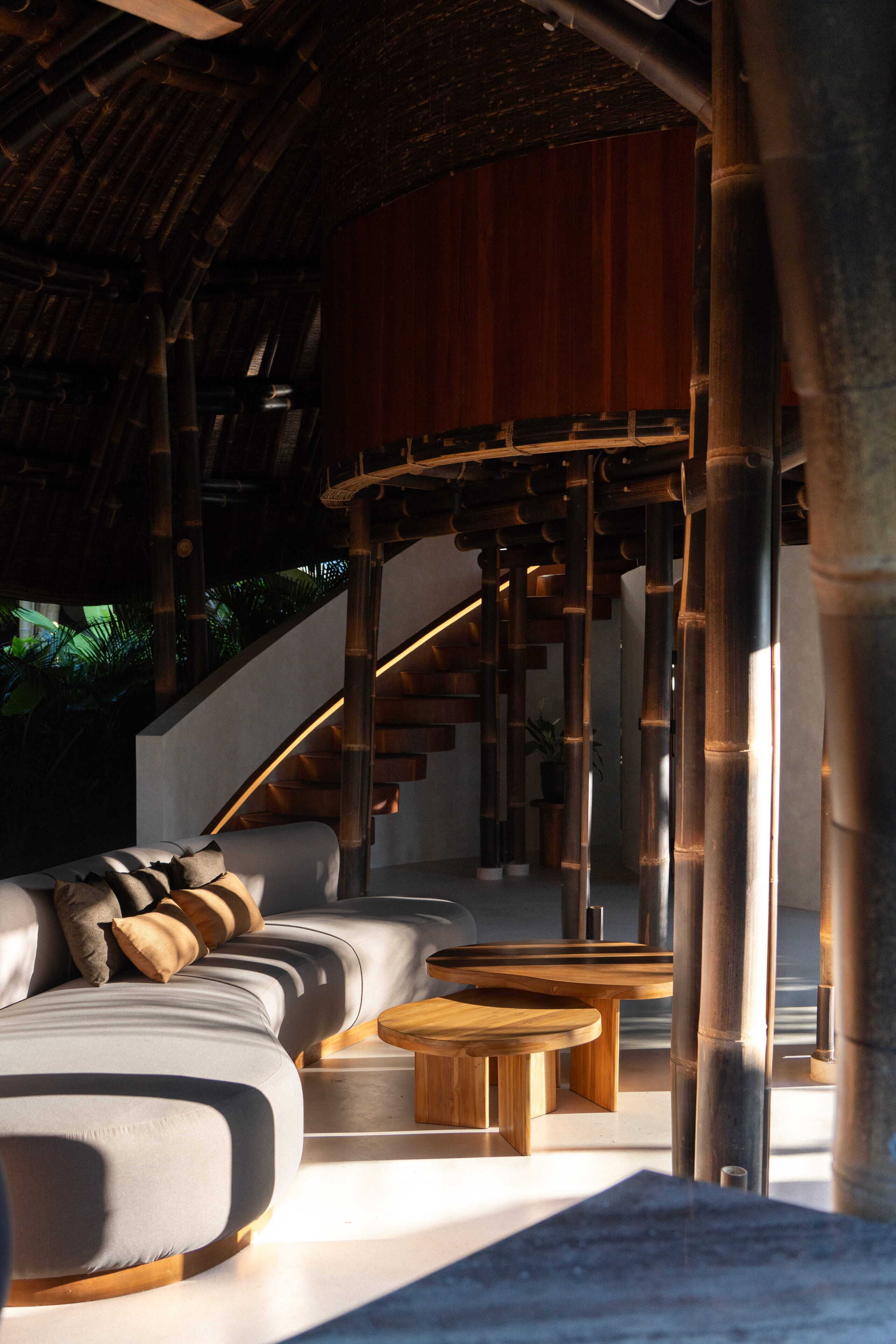A modern interior with a curved staircase, a sofa with cushions, and wooden tables.