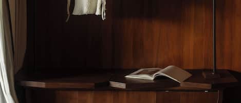 A room with a wooden floor, a white knitted sweater hanging on a metal rack, a book, and a glass on the floor.