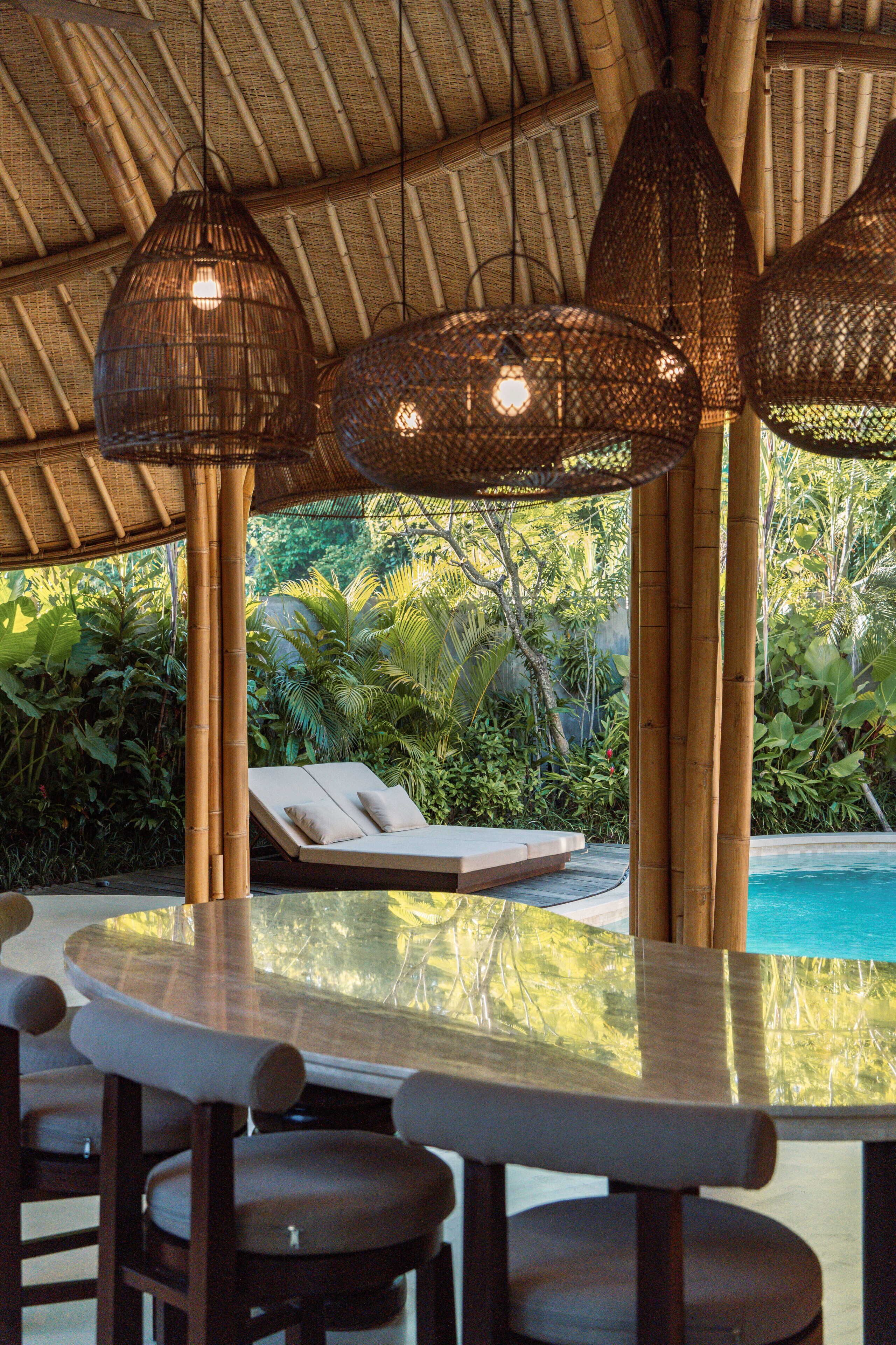A poolside area with a bamboo ceiling, lounge chairs, and a table with chairs.