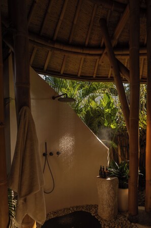A bathroom with a shower, a towel hanging, a stone base, and a potted plant. - Kaymana (Pecatu)