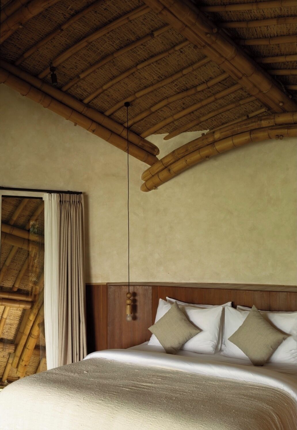 A room with a bed, wooden headboard, and a bamboo ceiling.