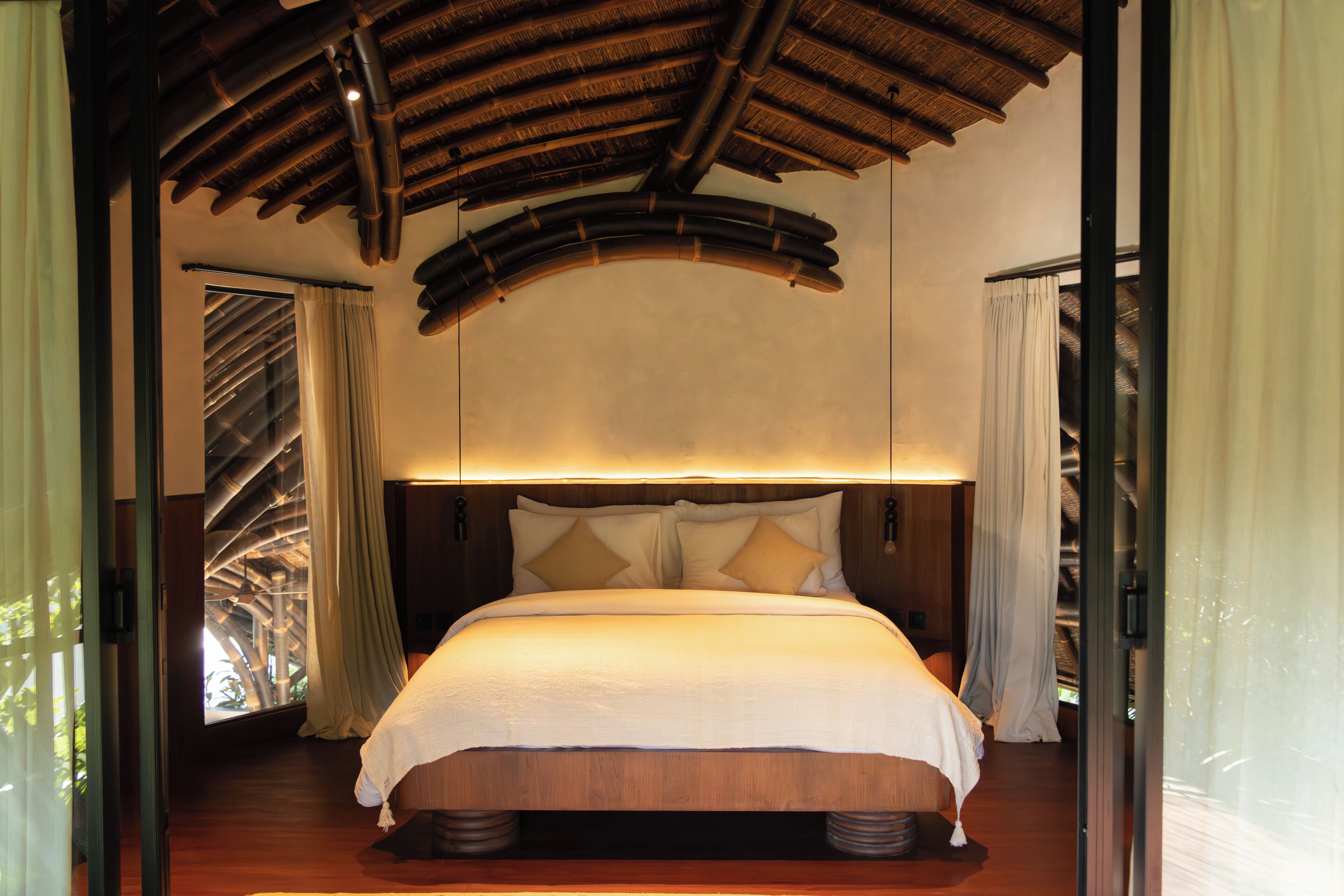 A room with a bed, wooden ceiling, and a view through a window.