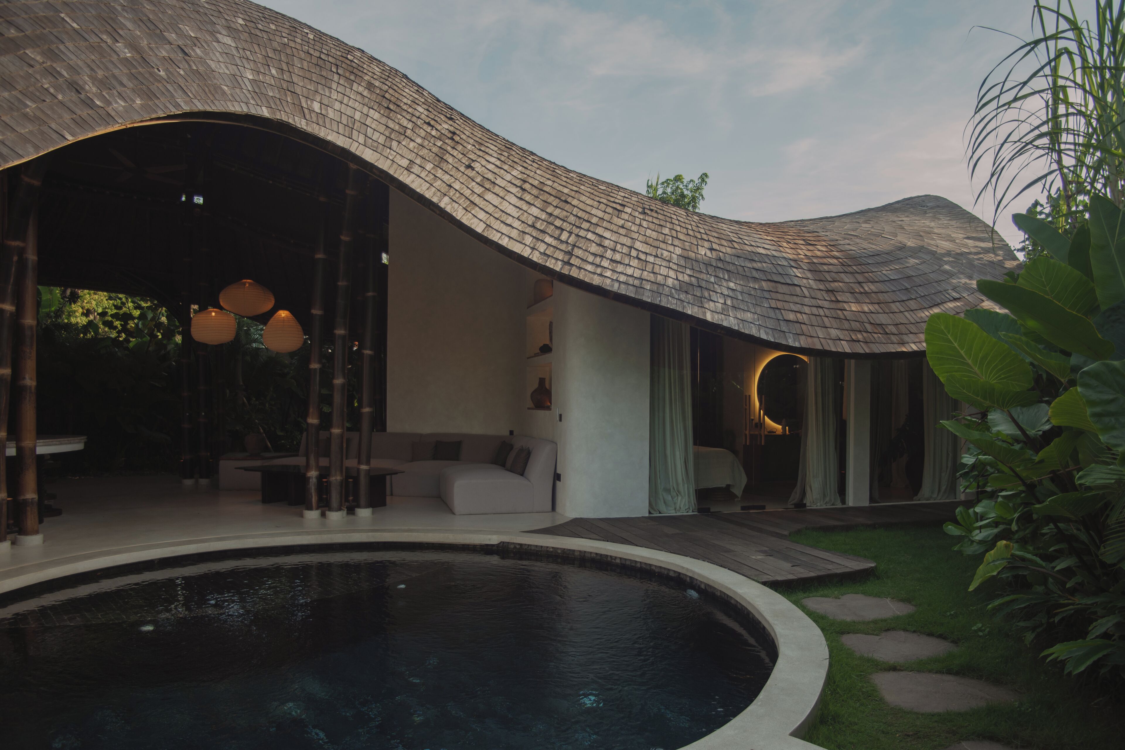 A modern house with a curved roof, a swimming pool, and a garden.