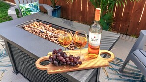 Een barbecue met spiezen vol eten, twee glazen wijn, een fles Sutter Home wijn en een houten dienblad met druiven.