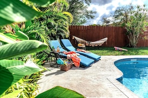 Ein Garten mit Swimmingpool, Liegestühlen, einer Hängematte und tropischen Pflanzen.