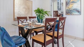 Un comedor con una mesa de vidrio, sillas de madera, una lámpara colgante y obras de arte en la pared.