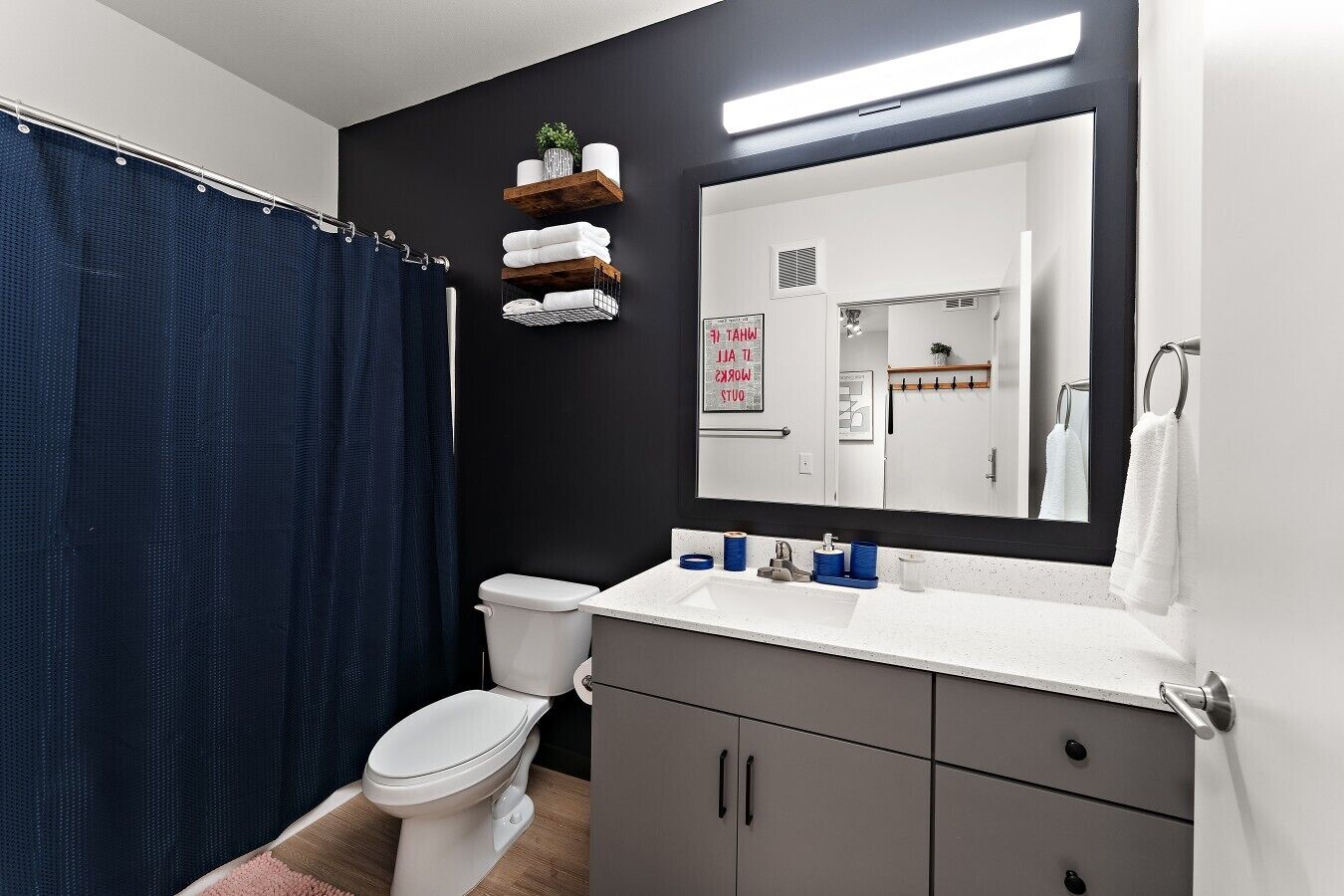Ein Badezimmer mit Toilette, Waschbecken mit blauen Seifenspendern, einem Spiegel und einem blauen Duschvorhang.