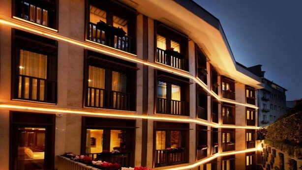 A multi-story hotel with balconies, a curved facade, and warm interior lighting. - Kate Hotel Special Class (Istanbul)