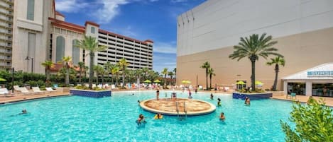 Una amplia piscina al aire libre con sillas de descanso y palmeras, rodeada por edificios de hotel.