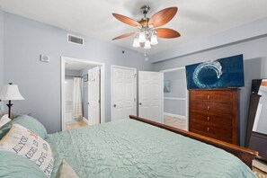 Ein Schlafzimmer mit einem Bett, einem Deckenventilator, einem Schminktisch und einem Bild an der Wand.