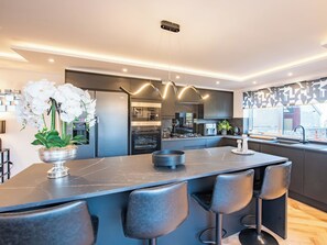 A modern kitchen with a central island, bar stools, a refrigerator, and a microwave. - Spey House by Interhome (Fochabers)