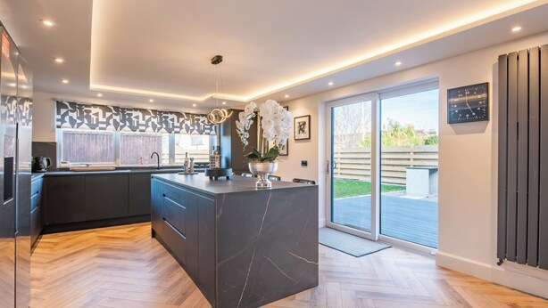 Une cuisine moderne dotée d’un grand îlot central, d’un four encastré et offrant une vue sur l’extérieur grâce à une porte vitrée.