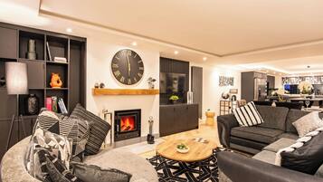 A modern living room with a fireplace, a large wall clock, and a dining area.