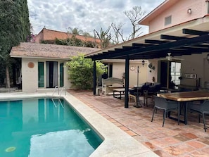 A swimming pool with a pergola, outdoor seating, and a small building with a tiled roof.