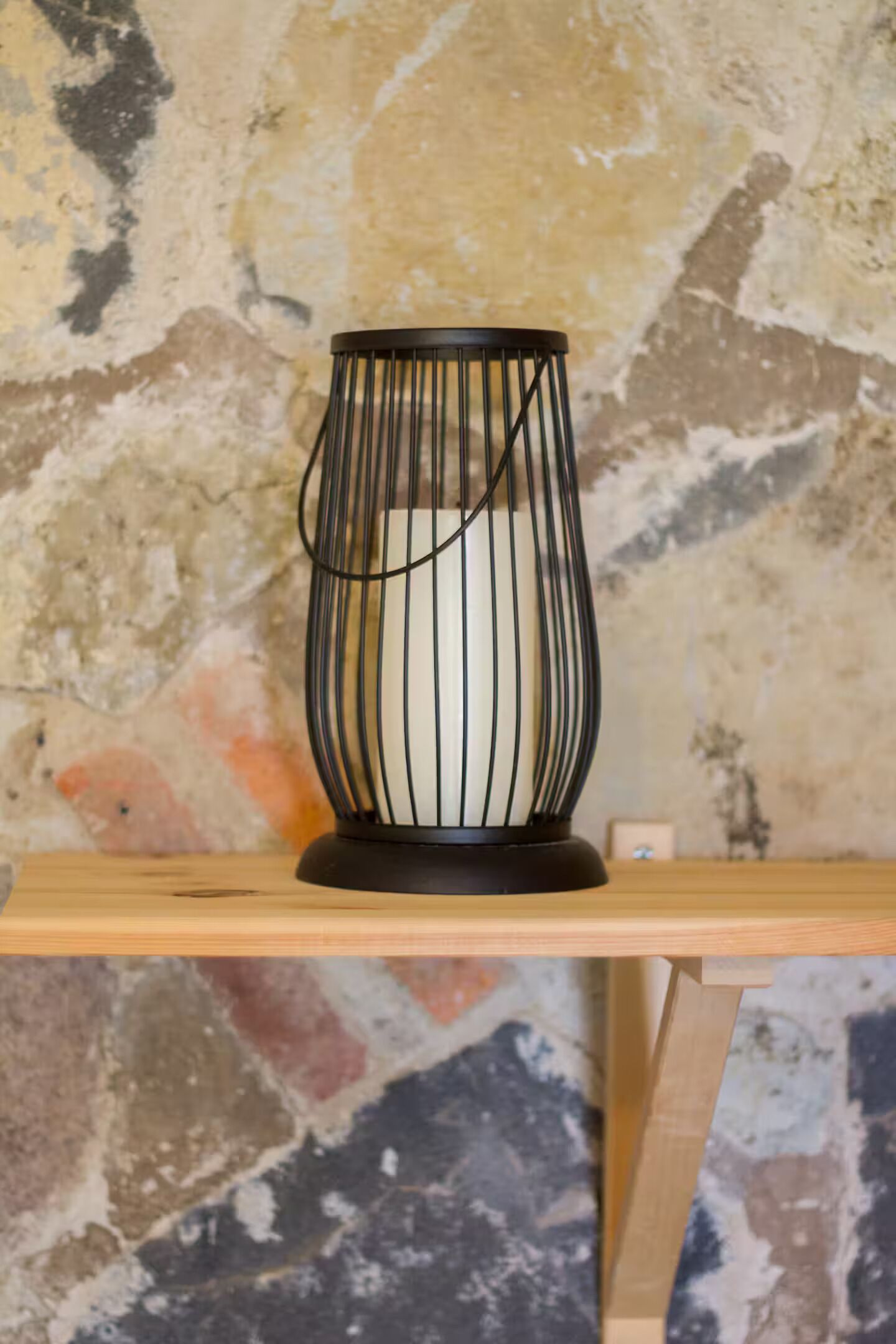 Un chandelier noir est posé sur une étagère en bois, adossé à un mur à la texture particulière.